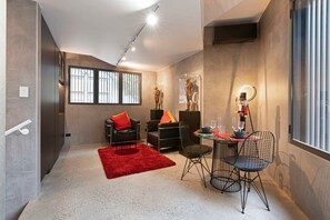 Un salon moderne avec un tapis rouge, des chaises noires, une petite table à manger et une grande fenêtre avec des stores.