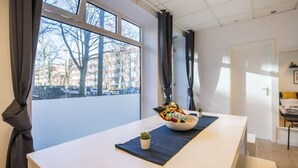 A modern hotel room with a large window, a dining table with a bowl of snacks, and a small plant.
