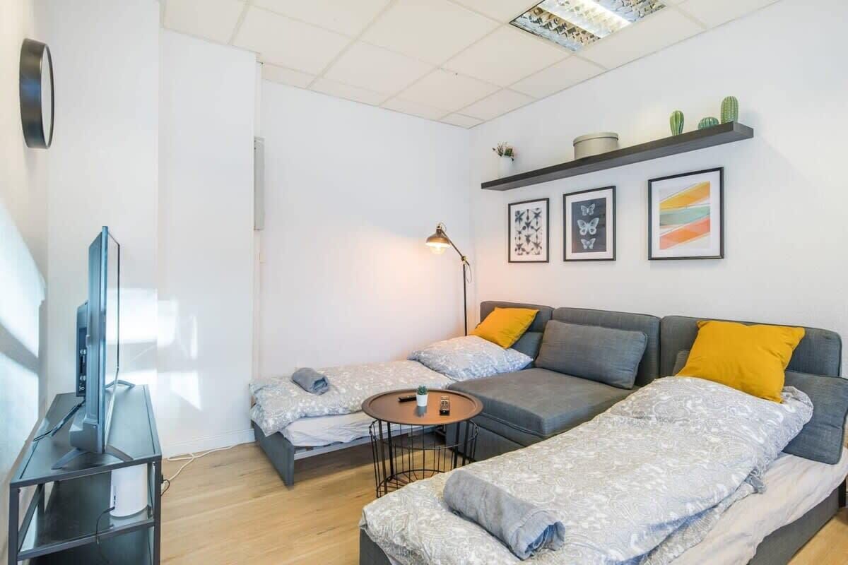 Un salon moderne avec un canapé gris, deux lits simples, une télévision et une petite table.
