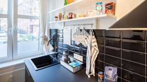 A modern kitchen with black tiled backsplash, a window with a view of buildings, and shelves with various food items.