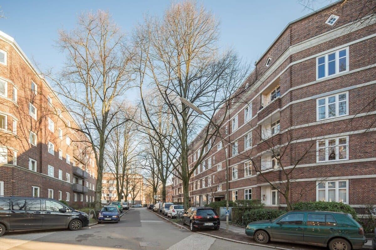 Una calle residencial flanqueada por edificios de apartamentos de ladrillo, coches estacionados y árboles sin hojas.
