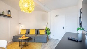 Un salon moderne avec un canapé gris, des coussins jaunes, une table basse ronde et un grand luminaire décoratif.