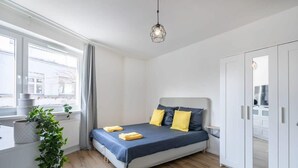 Um quarto com cama, janela, planta e guarda-roupa.