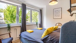 Ein Schlafzimmer mit einem Bett, einem Sessel, einem Fenster mit Vorhängen, einer Heizung und einer Pendelleuchte.