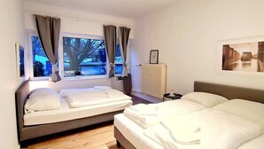 A modern bedroom with two beds, a large window with curtains, a radiator, and a framed picture on the wall. - Apartment 1 Hamburg Winterhude (Hamburg)