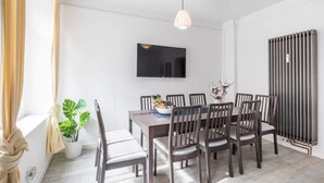 Un comedor moderno con una mesa y sillas de madera, una planta en maceta y un televisor montado.