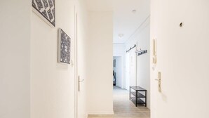 Un pasillo con piso de madera, paredes blancas y dos puertas. En las paredes, hay cuadros enmarcados en blanco y negro.