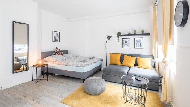 Un dormitorio moderno con una cama, un sofá, una mesita redonda y un espejo.
