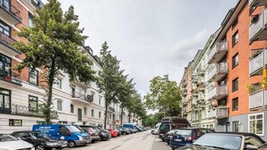 Calle flanqueada por edificios residenciales de varios pisos, coches aparcados y una furgoneta azul con señalización visible.