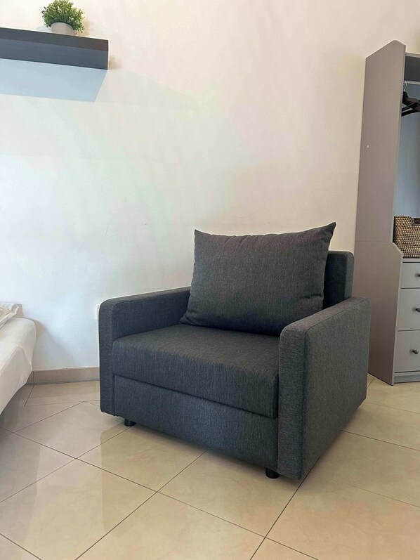 A grey armchair with a cushion in a room with a tiled floor and a white wall. - Gemütliche Wohnung in Hamburg Hammerbrook (Hamburg)