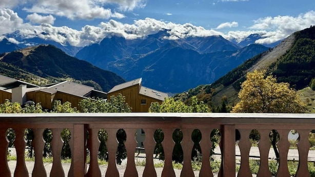 A mountain view with a wooden building and a balcony with a wrought iron railing.