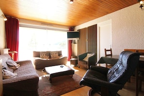 Un salon avec un plafond en bois, un canapé, une table basse, un fauteuil en cuir et un coin repas avec une table et des chaises.