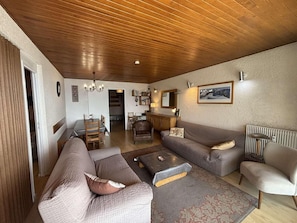 Un salon chaleureux avec un plafond en bois, un canapé, une table basse et un coin repas comprenant une table et des chaises.