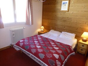 Une chambre à coucher avec un lit, deux tables de chevet, un radiateur et une fenêtre avec des rideaux.