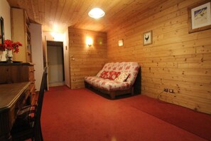 A cozy room with wooden walls, a red carpet, a floral sofa, and a wooden dresser.