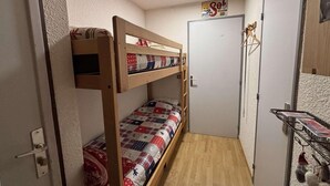 A small, narrow room with a bunk bed, a door, and a small kitchenette area. - 100m from resort center, 1st floor, balcony, tv, 25m², Alpe d'Huez (L'Alpe d'Huez)