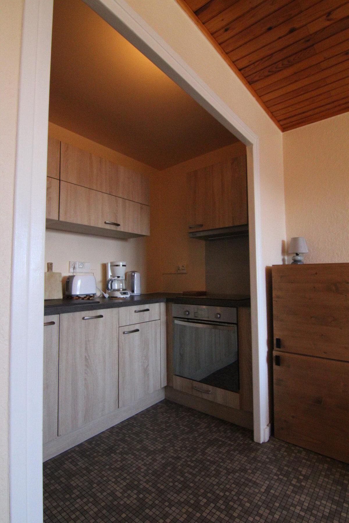 A compact kitchen with light wood cabinets, a built-in oven, and a coffee maker.