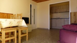 Een kamer met een houten eettafel en stoelen, een roze bank en een keukenhoek met kastjes en een spoelbak.