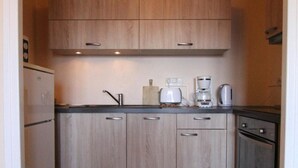 Een compacte keuken met lichte houten kastjes, een koelkast, een broodrooster en een koffiezetapparaat.