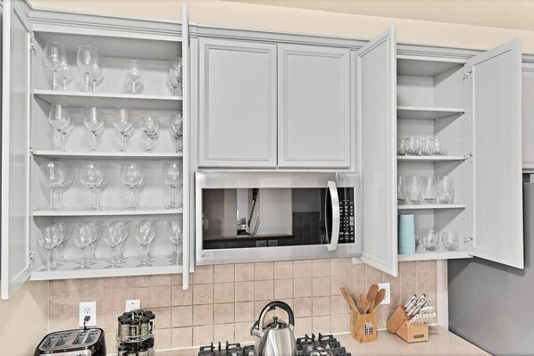 Una cocina con armarios blancos, microondas, hervidor y tostadora.