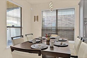 Comedor con una mesa redonda preparada para seis personas, rodeada de sillas blancas.