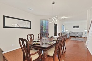 Un comedor con una mesa y sillas de madera, un espejo grande, y vista a una sala de estar con un sofá y una escalera.