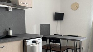 A compact kitchen with a dishwasher, a dining table with chairs, a TV mounted on the wall, and a clock. - 80m from shops, 3rd floor, tv, ski locker, 24m², Alpe d'Huez (L'Alpe d'Huez)