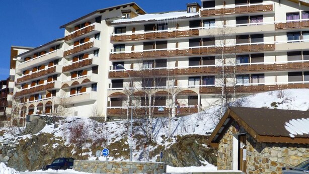 A multi-story hotel with balconies, stone walls, and a snowy landscape. - 80m from shops, 3rd floor, tv, ski locker, 24m², Alpe d'Huez (L'Alpe d'Huez)