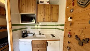 Una cucina compatta con mobili in legno, un forno a microonde, un lavello, una macchina per caffè e un piccolo frigorifero.