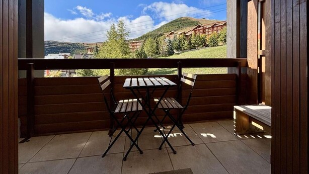 Un balcone con tavolo e sedie di legno, vista su una montagna e edifici sullo sfondo.