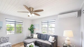 Un soggiorno con un divano componibile, una ventola a soffitto, due finestre e un condizionatore.