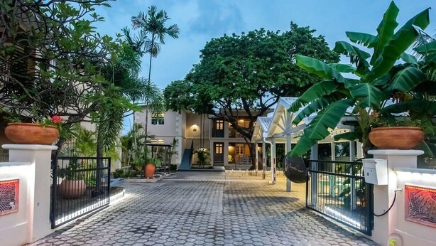 Un vialetto lastricato con cancello che conduce a un edificio con un albero grande e piante in vaso.