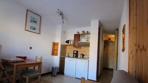 A compact living space with a kitchenette, a dining area with a wooden table and chairs, and a small trash bin.