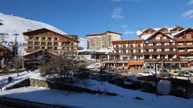 A snow-covered town with multi-story buildings, including a hotel with balconies and a ski lift in the background.