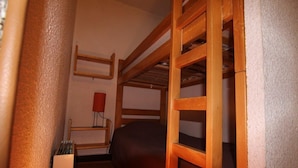 A small, narrow room with a bunk bed, a bedside table, and a red lamp.