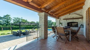An outdoor patio with a stone fireplace, a pool, and a covered seating area. - Modern Villa Elida with pool (Heki)
