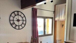 A dining area with a wooden table, chairs, and a wall clock. - 20m from ski slopes, 6th floor, tv, ski locker, 27m², Alpe d'Huez (L'Alpe d'Huez)