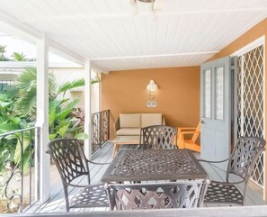 A covered outdoor seating area with a table and chairs, a sofa, and a wall-mounted lamp.