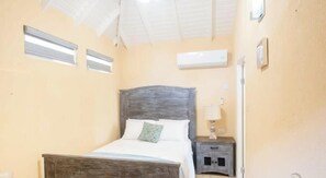 A bedroom with a wooden bed, a nightstand, an air conditioning unit, and a ceiling fan.