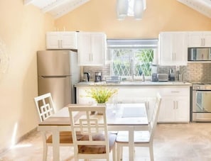 A kitchen with white cabinets, a stainless steel refrigerator, a stove, and a dining area with a table and chairs. - Near Dover Beach Apt with Private Patio & Parking (Oistins)