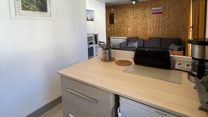 Uma cozinha compacta com bancada de madeira, geladeira e um pequeno espaço de refeições com sofá.