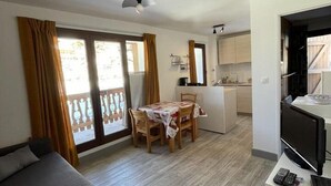 Espaço compacto com sofá, mesa de jantar e cadeiras, cozinha e varanda com cortinas.