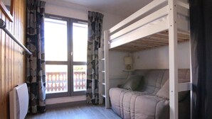Um quarto com cama de solteiro e beliche, um sofá, uma janela com cortinas e um radiador.
