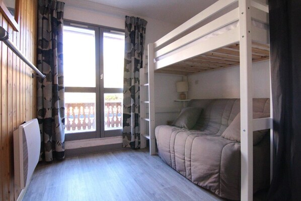 A room with a bunk bed, a sofa, a window with curtains, and a radiator.