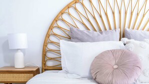 A bed with a rattan headboard, white bedding, and a bedside lamp on a wooden nightstand.