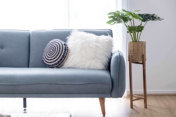Un canapé gris agrémenté de coussins à motifs et moelleux, un support à plantes en osier et un plancher en bois.