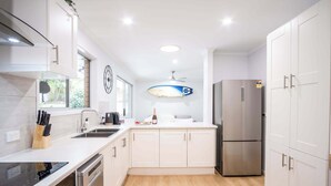 A modern kitchen with white cabinetry, a stainless steel refrigerator, and a surfboard decoration.