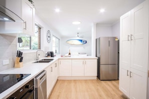 Una cucina moderna con mobili bianchi, un frigorifero in acciaio inossidabile e una decorazione a forma di tavola da surf.