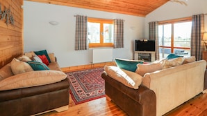 A cozy living room with wooden walls and ceiling, a brown leather sofa, a beige sofa, a red patterned rug, and a television. - Osprey Lodge (Lincoln)