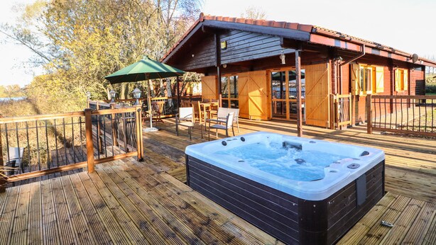 A wooden deck with a hot tub, outdoor seating, and a covered area with wooden doors. - Osprey Lodge (Lincoln)